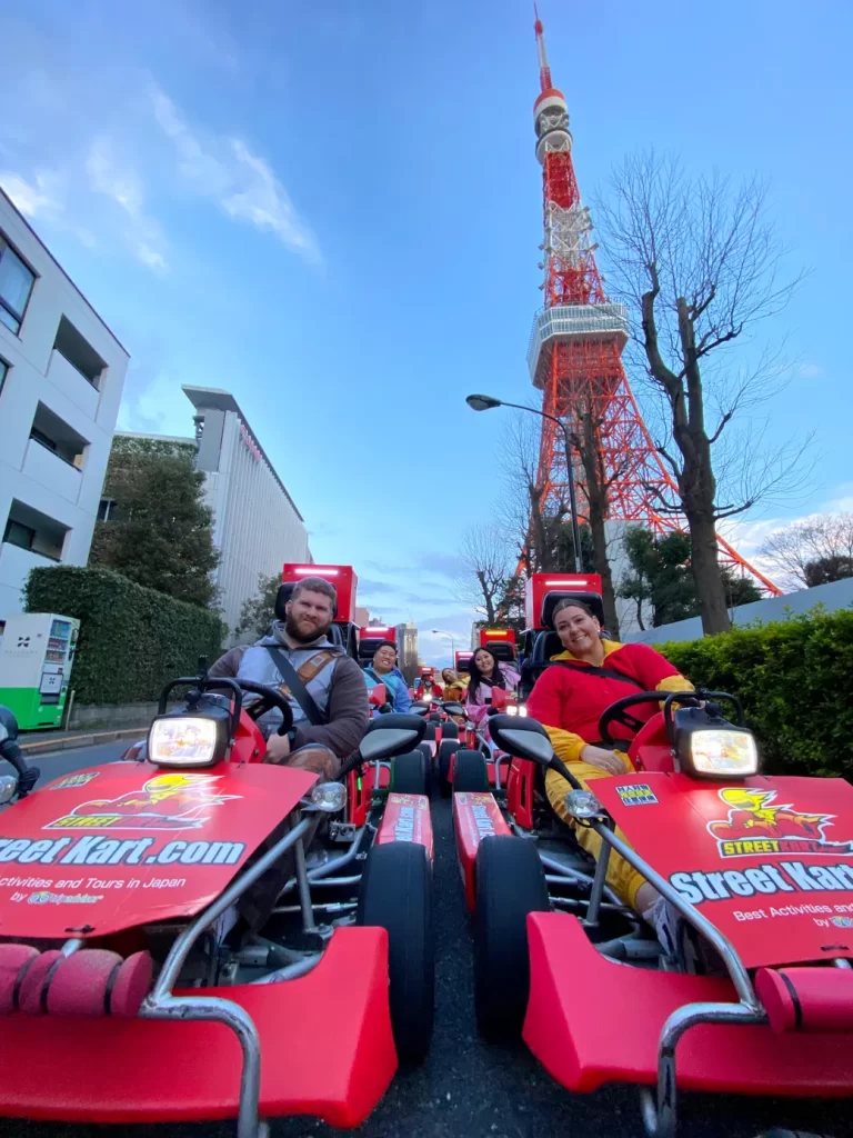 Group of people in red go-karts riding on a street with Tokyo Tower in the background.